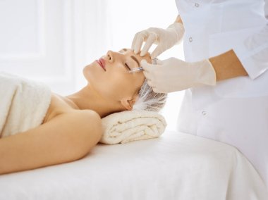 Güzel bir kadın kapalı gözlerle güzellik iğneleri yaptırıyor. Güzellik uzmanı elleri şırıngayla kadın yüzüne güzellik prosedürü uyguluyor. Kozmetik tıp ve cerrahi konsepti