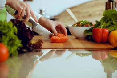 Mutfakta pişen bilinmeyen insan elleri. Kırmızı domatesleri dilimleyen kadın. Sağlıklı yemek ve vejetaryen gıda konsepti.