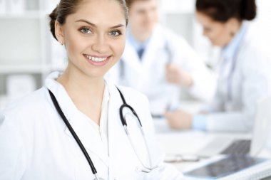 Happy smiling woman-doctor sitting and looking at camera at meeting with medical staff . Medicine concept clipart