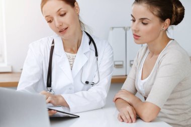 Doktor ve hasta güneşli klinikte oturup sağlık muayenesi sonuçlarını tartışıyor.