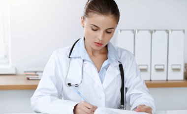 Kadın doktor güneşli klinikte oturuyor ve çalışıyor. Kadın doktor portresi. Tıp konsepti