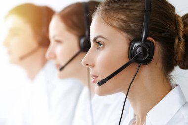 Merkezi ara. Güzel genç bir kadın güneşli ofisteki müşterilere yardım etmek için kulaklık ve bilgisayar kullanıyor. İş konsepti