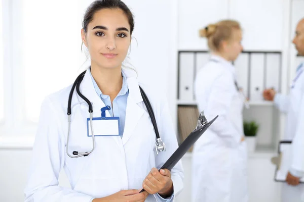 医生妇女在诊所与同事为背景。拉美裔或拉丁裔美国医学工作人员 — 图库照片
