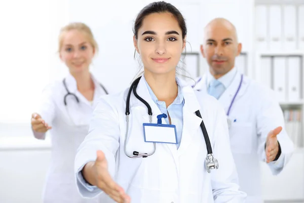 Dottoressa che mostra OK in clinica con i colleghi sullo sfondo. Personale ispanico o latino americano in medicina — Foto Stock