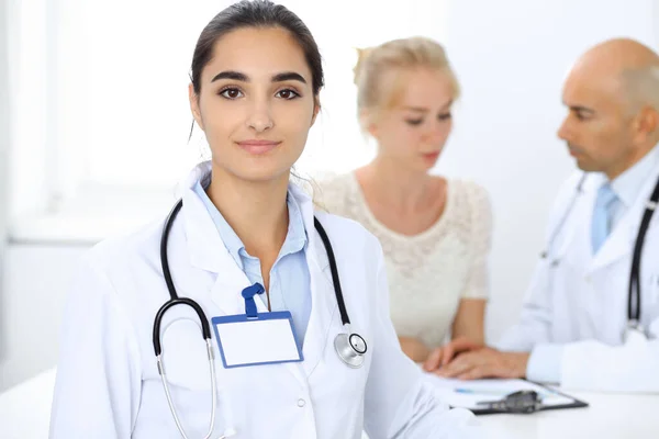 医生妇女在诊所与同事为背景。拉美裔或拉丁裔美国医学工作人员 — 图库照片