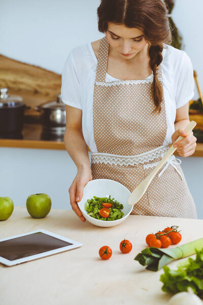 Молодая брюнетка готовит на кухне. Домохозяйка держит в руке деревянную ложку. Концепция питания и здоровья