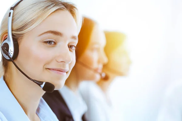 Group of diverse phone operators at work in sunny office. Handsome business woman with headphones consulting clients. Call center and business people concept