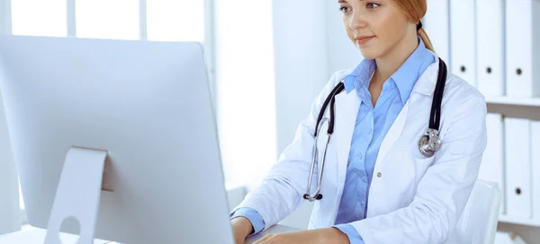 Młoda kobieta lekarz w szpitalu patrząc na pulpit komputera monitora. Lekarz kontroluje historię leczenia i wyniki badań. Koncepcja medycyny i opieki zdrowotnej — Zdjęcie stockowe