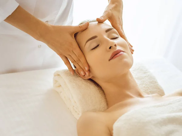 Красива жінка насолоджується масажем обличчя з закритими очима в спа-центрі. Розслаблююча концепція лікування в медицині — стокове фото