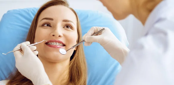 Diş hekiminde dişçi tarafından incelenen diş telleriyle gülümseyen genç bir kadın. Sağlıklı diş ve ilaç konsepti — Stok fotoğraf