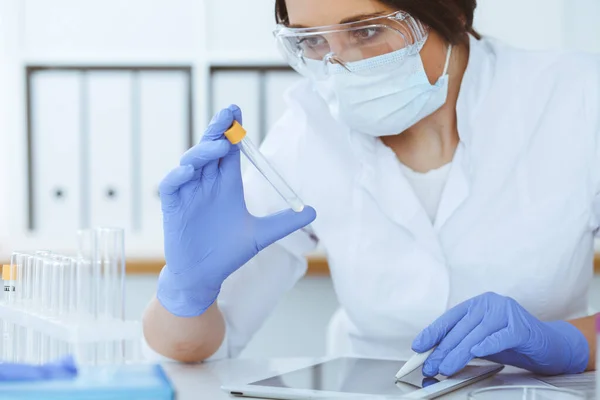 Primer plano de la científica profesional en gafas protectoras haciendo experimento con reactivos en laboratorio. Concepto de medicina e investigación — Foto de Stock