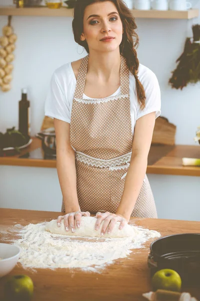 Mladá brunetka žena vařící pizzu nebo ručně dělané těstoviny v kuchyni. Hospodyně připravuje těsto na dřevěném stole. Dietní, stravovací a zdravotní koncepce — Stock fotografie