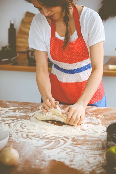 Mladá brunetka žena vařící pizzu nebo ručně dělané těstoviny v kuchyni. Hospodyně připravuje těsto na dřevěném stole. Dietní, stravovací a zdravotní koncepce — Stock fotografie