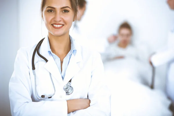 Жінка-лікар посміхається на фоні з пацієнтом в ліжку і двома лікарями — стокове фото