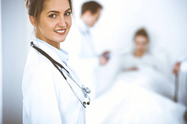 Female doctor smiling on the background with patient in the bed and two doctors