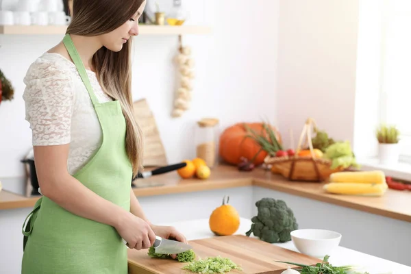 Mooie vrouw gekleed in schort is koken maaltijd in zonnige keuken — Stockfoto