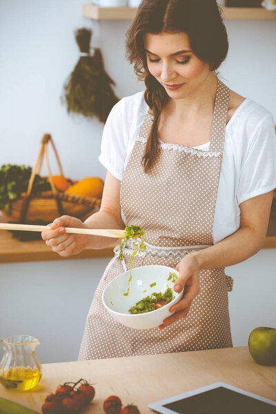 Молодая брюнетка готовит на кухне. Домохозяйка держит в руке деревянную ложку. Концепция питания и здоровья