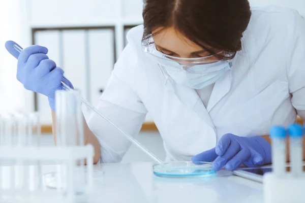 Close-up of professional female scientist in protective eyeglasses making experiment with reagents in laboratory. Medicine and research concept Stock Picture
