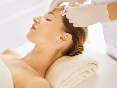 Güzel bir kadın kapalı gözlerle güzellik iğneleri yaptırıyor. Güzellik uzmanı elleri şırıngayla kadın yüzüne güzellik prosedürü uyguluyor.