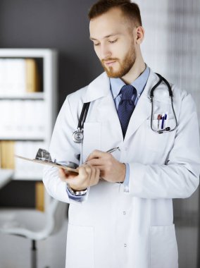 Dost canlısı kızıl sakallı doktor çalışma yerindeki klinikte panoya yazı yazıyor. Hastanede mükemmel bir tıbbi hizmet. Tıp konsepti