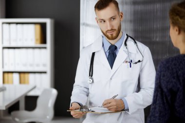 Dost canlısı kızıl sakallı doktor ve hasta kadın klinikte otururken sağlık muayenesini tartışıyorlar. Mükemmel tıbbi hizmet ve tıp konsepti