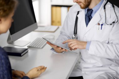 Bilinmeyen kızıl sakallı doktor ve hasta kadın klinikte oturup tablet bilgisayar kullanırken sağlık muayenesini tartışıyorlar. Tıp konsepti