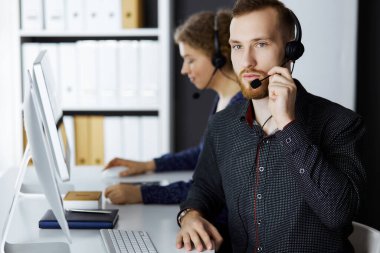 Modern ofiste otururken kulaklıkla konuşan kızıl sakallı bir iş adamı. Çağrı merkezinde çeşitli insanlar var. Tele pazarlama ve müşteri hizmetleri