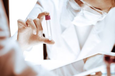 Koronavirüs salgını. Koruyucu gözlüklü profesyonel kadın bilim adamı laboratuarda reaktörlerle araştırma tüpü kullanıyor. İlaç ve virüs koruması kavramları
