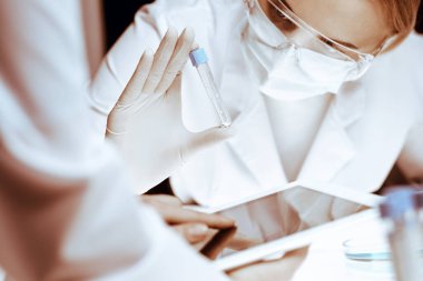 Koronavirüs salgını. Koruyucu gözlüklü profesyonel kadın bilim adamı laboratuarda reaktörlerle araştırma tüpü kullanıyor. İlaç ve virüs koruması kavramları