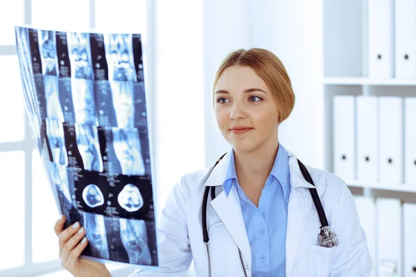 Doctor woman examining x-ray picture near window in hospital. Surgeon or orthopedist at work. Medicine and healthcare concept. Blue colored blouse of a therapist looks good — Stock Photo, Image