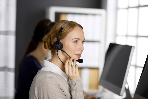 Femme d'affaires amicale parlant par casque dans le bureau. Centre d'appels et divers groupes de personnes en affaires — Photo