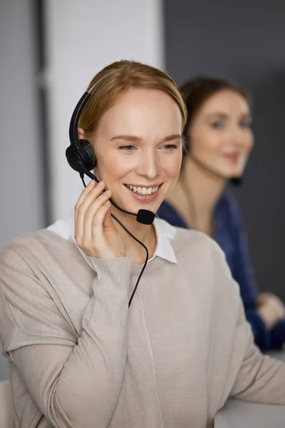 Friendly businesswoman talking by headset in office. Call center and diverse people group in business — Stock Photo, Image