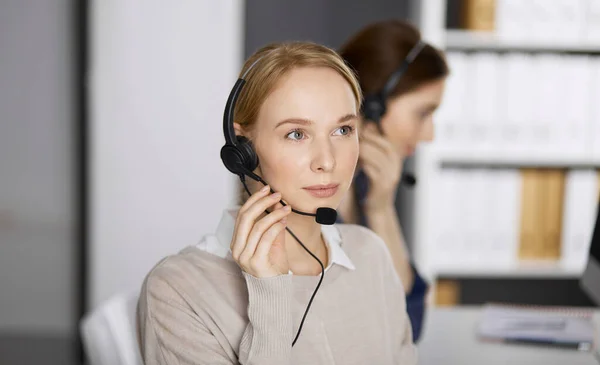 Femme d'affaires amicale parlant par casque dans le bureau. Centre d'appels et divers groupes de personnes en affaires — Photo