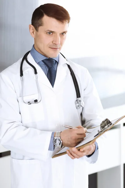 Doctor man using clipboard for filling up medication history records. Perfect medical service in clinic. Physician at work in hospital. Medicine and healthcare concepts — Stock Photo, Image