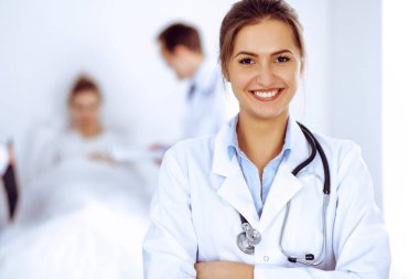 Arka planda gülümseyen kadın doktor, yatakta hasta ve iki doktor.