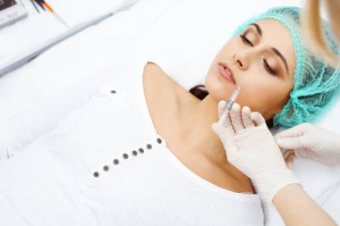 Profesyonel kozmetik uzmanı yüzüne ve dudaklarına iğne yapıyor. Genç bir kadın, yüz hatları ya da büyütme için doldurucu iğneyle doldurulur. Yaşlanma, gençleşme ve hidrasyon prosedürleriyle yüzleş