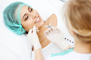 Profesyonel kozmetik uzmanı yüzüne ve dudaklarına iğne yapıyor. Genç bir kadın, yüz hatları ya da büyütme için doldurucu iğneyle doldurulur. Yaşlanma, gençleşme ve hidrasyon prosedürleriyle yüzleş