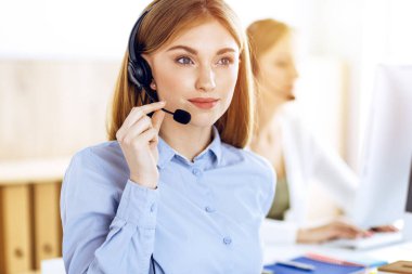 Çağrı merkezi operatörünün güneşli ofisindeki portresi. Kulaklık takmış bir grup insan müşterilere yardım etmeye hazır. İş konsepti