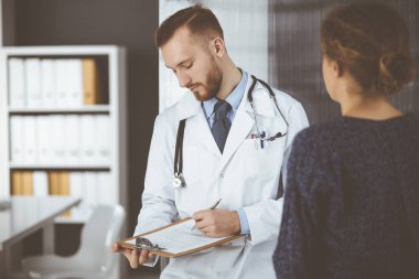 Dost canlısı kızıl sakallı doktor ve hasta kadın klinikte otururken sağlık muayenesini tartışıyorlar. Tıp konsepti