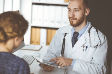 Dost canlısı kızıl sakallı doktor ve hasta kadın klinikte otururken sağlık muayenesini tartışıyorlar. Tıp konsepti