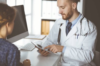 Dost canlısı kızıl sakallı doktor ve hasta kadın klinikte otururken sağlık muayenesini tartışıyorlar. Tıp konsepti