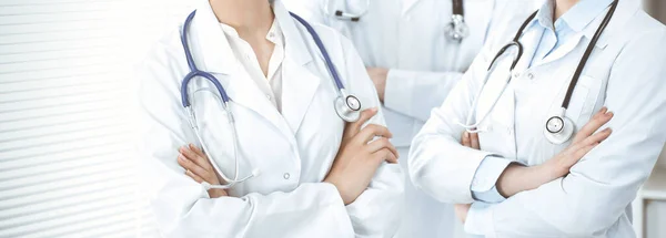 Unknown woman-doctor standing straight with arms crossed in clinic, close-up. Medical team ready to stop coronavirus pandemic. Medicine concept