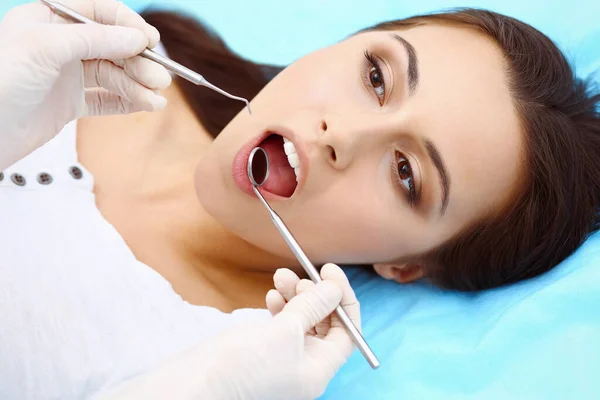 Young female patient visiting dentist office.Beautiful woman with healthy straight white teeth sitting at dental chair with open mouth during oral checkup while doctor working at teeth — Stock Photo, Image