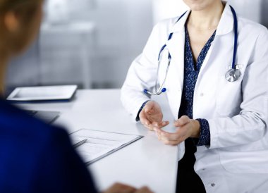 Bilinmeyen kadın-doktor, klinikteki dolapta birlikte otururken hastasıyla teşhisi hakkında konuşuyor. İşyerindeki doktor, yakın plan. Mükemmel bir tıbbi hizmet.