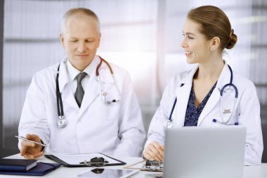 Yaşlı doktor ve bayan meslektaşı güneşli klinikte çalışırken güncel hastalık terapisini tartışıyorlar. Tıpta takım çalışması