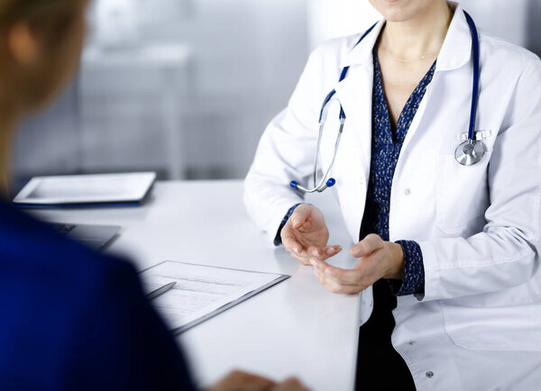 Неизвестная женщина-врач разговаривает со своим пациентом о своем диагнозе, сидя вместе за столом в кабинете в клинике. Врач на рабочем месте, крупным планом. Перфектное медицинское обслуживание в