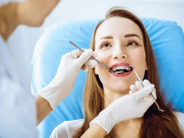 Diş hekiminde dişçi tarafından muayene edilen diş telleriyle gülümseyen genç bir kadın. Sağlıklı dişler ve tıbbi bakım konsepti — Stok fotoğraf