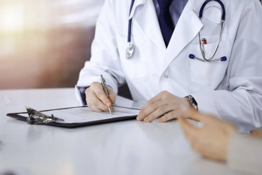 Bilinmeyen bir erkek doktor ve hasta kadın karanlık bir klinikte otururken bir şey tartışıyorlar ve arka planda pano kullanıyorlar.