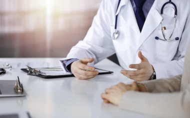 Bilinmeyen bir erkek doktor ve hasta kadın karanlık bir klinikte otururken bir şey tartışıyorlar, arka planda ışık parlıyor. Ellerin yakın çekimi