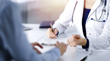 Bilinmeyen kadın doktor, bir klinikteki güneşli dolapta otururken hastasına bazı antibiyotikler yazıyor. Steteskoplu kadın doktor panoya yazı yazıyor.